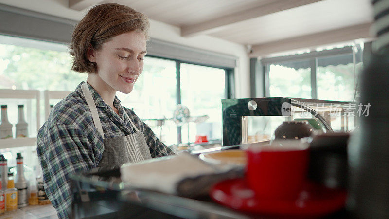 Close up. Young barista making coffee for customers at the Café. Entrepreneur or employee standing behind the counter ready to serve customers or barista take the order in cafe. Young females business owner or manager working in coffee shop.